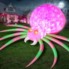 an inflatable pink and green spider with glowing eyes on the grass near a house