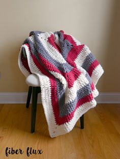 a crocheted blanket sitting on top of a chair next to a wooden floor