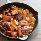 a pan filled with meat and vegetables on top of a wooden table