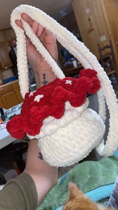 a person holding up a knitted basket with a cat in it