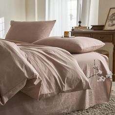 a bed with pink sheets and pillows on top of it in a room next to a window