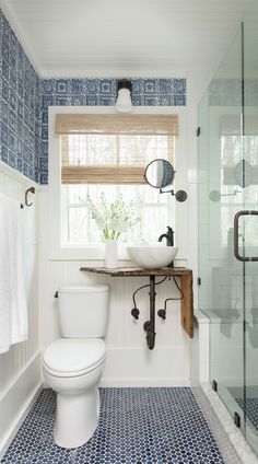 a white toilet sitting next to a walk in shower under a bathroom window with blue tiles on the floor