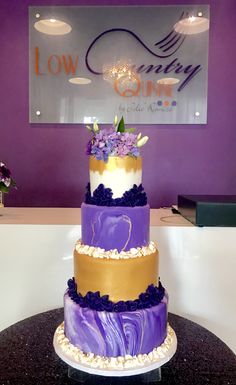 three tiered cake sitting on top of a table in front of a purple wall