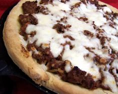 a pizza with meat and cheese on it sitting on a table next to a red cloth