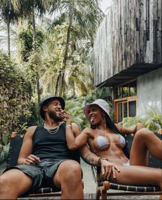 a man and woman sitting next to each other on a bench in front of some palm trees