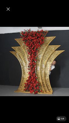 a large gold sculpture with red flowers on it's sides and a woman in the background