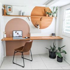 a desk with a laptop on it in front of a potted plant next to a window