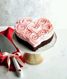 a heart shaped cake with pink frosting on a white plate next to a knife