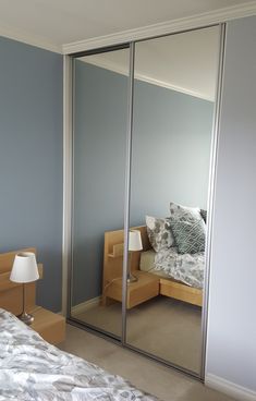 a bed sitting next to a mirrored wall in a bedroom under a light blue sky