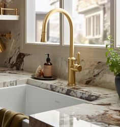 a kitchen sink with gold faucet and marble counter top next to a window