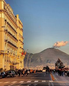 people are walking down the street in front of tall buildings with a mountain in the background