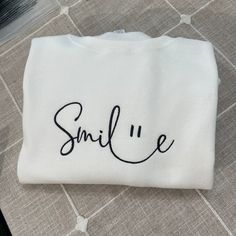 Smile Embroidered Sweatshirt. Hello there! Please message me if you have any additional questions or want to change thread colors. We are a family-run Etsy page; my husband and I make all orders from home. You can also send us a message if you would like a custom sweatshirt/t-shirt with whatever words and images, and we will see if we can accommodate your order! HOW TO ORDER - Please Choose the SIZE and COLOR From Drop Down Menu. MATERIAL - We use JerZees as our blanks; I may sometimes substitut White Letter Embroidery Sweatshirt For Loungewear, White Sweatshirt With Letter Embroidery For Loungewear, Winter Smiley Face Crew Neck Sweatshirt, Funny White Relaxed Fit Sweatshirt, White Relaxed Fit Funny Sweatshirt, Fall Crew Neck Sweatshirt With Smiley Face, Fall Smiley Face Crew Neck Sweatshirt, Trendy Letter Embroidery Sweatshirt For Loungewear, Smiley Face Crew Neck Tops For Loungewear