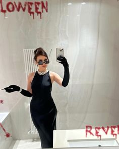 a woman in a black dress is taking a selfie with her cell phone and gloves