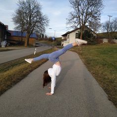 a woman doing a handstand on the road in front of some houses and trees