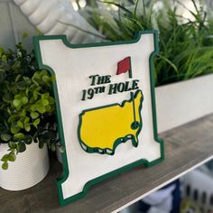 a green and white sign that says the 19th hole in front of some potted plants