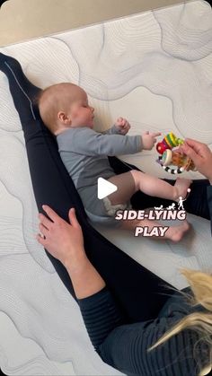 a woman laying on top of a bed with a baby in her lap holding a toy