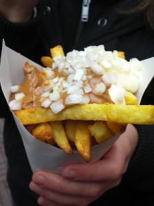 a person holding a paper container filled with french fries and sauce on top of it