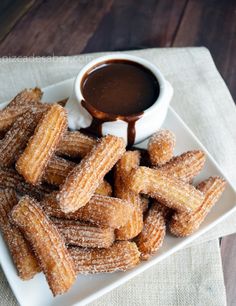 some sugary churros on a white plate with dipping sauce in the middle