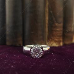 a white diamond ring sitting on top of a purple velvet covered table next to books