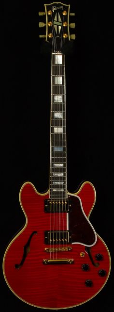 a red electric guitar sitting on top of a black background with its neck and frets