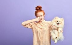 a woman holding a small white dog in her right hand and looking at the camera