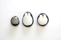 three penguins sitting on top of each other in black and white eggs with yellow beaks