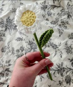 a crocheted flower is being held by someone's hand on a bed