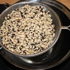 a metal pan filled with black eyed peas on top of a stove burner next to a wooden table