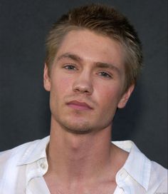 a close up of a person wearing a white shirt and looking at the camera with a serious look on his face