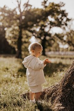 a small child standing next to a tree in a field with grass and trees behind it