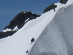 three people climbing up the side of a snow covered mountain