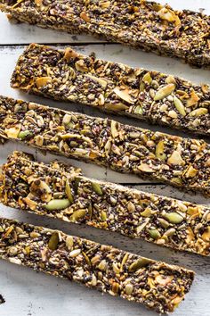 five homemade granola bars lined up on a white wooden surface with nuts and seeds