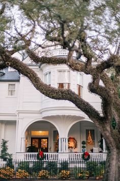 a white house with christmas decorations on the front porch and trees in front of it