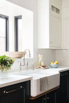 a kitchen with black cabinets and white countertops has a bowl of lemons on the sink