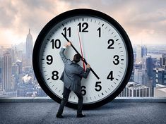 a man in a suit is holding on to a large clock with the city skyline behind him