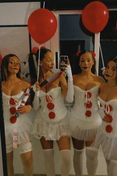 four women dressed in white and red posing for a photo with balloons on the wall behind them