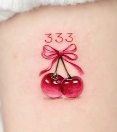 a tattoo with two cherries and a bow on the side of her thigh that reads 33 3