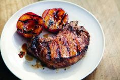 grilled pork chops and peaches on a white plate sitting on a wooden table