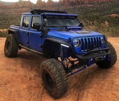 a blue jeep parked on top of a dirt field next to mountains and clouds in the sky