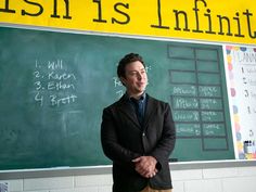 a man standing in front of a blackboard with writing on it and another chalk board behind him