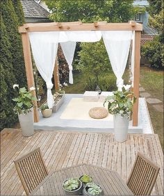 an outdoor table and chairs are set up on the deck with white drapes over it