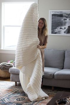 a woman standing next to a couch covered in a white crochet knitted blanket