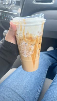 a person holding up a starbucks cup in their hand while sitting in the drivers seat