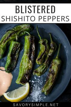 some green peppers on a blue plate with a lemon wedge and sauce in the middle