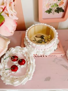 there are cherries in the bowl on the table next to pink flowers and plates