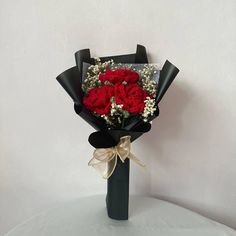 a bouquet of red carnations and baby's breath wrapped in black paper