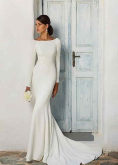 a woman standing in front of a blue door wearing a white dress and holding a bouquet