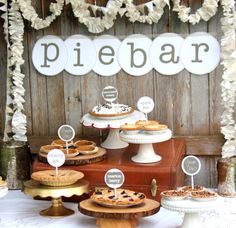 a table topped with pies and cakes next to a wooden wall covered in paper flowers