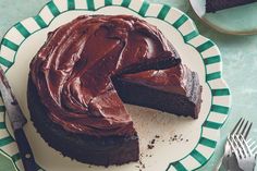 a chocolate cake on a green and white plate with one slice cut from the cake