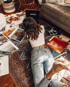 a woman is sitting on the floor surrounded by books and magazines in her living room